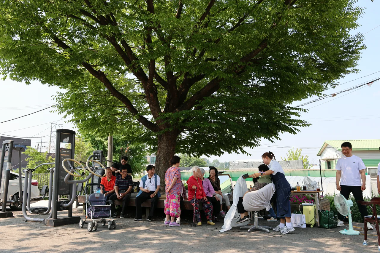 마을 느티나무 그늘 아래 마련된 야외 미용봉사 자리와 차례를 기다리는 마을 어르신들